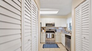 Uma cozinha estreita com armários brancos, micro-ondas, forno e lava-louças.