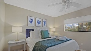 Quarto com cama, duas mesas de cabeceira, ventilador de teto e quadros nas paredes.