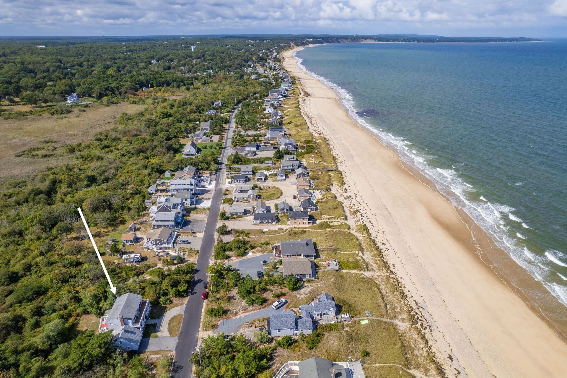 An aerial view of a coastal residential area with houses along the beach and a road running parallel to the shore.