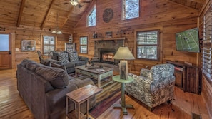 A log cabin interior with a fireplace, leather sofas, a television, and a stone fireplace mantel.