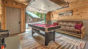 A cozy room with a pool table, a sofa, and a sign indicating outdoor activities like fishing and kayaking.