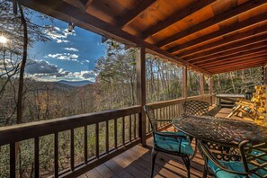 A wooden deck with a table and chairs, overlooking a forested landscape. - Treehouse Hideaway - Pet Friendly | Hot Tub | Game Room (Cherry Log)