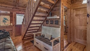 A wooden cabin interior with a wooden staircase, a white bench with a cushion, and a map on the wall. - Treehouse Hideaway - Pet Friendly | Hot Tub | Game Room (Cherry Log)