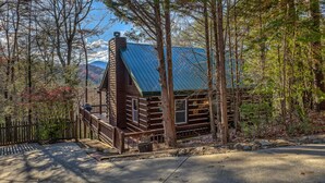 A rustic cabin with a wooden exterior, a sloped roof, and a porch. - Treehouse Hideaway - Pet Friendly | Hot Tub | Game Room (Cherry Log)