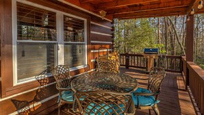 A wooden deck with a round table and chairs, large windows, and a view of trees. - Treehouse Hideaway - Pet Friendly | Hot Tub | Game Room (Cherry Log)