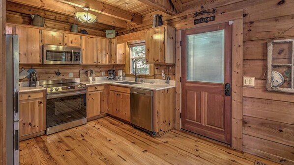 A wooden cabin kitchen with a stainless steel refrigerator, oven, microwave, and sink.