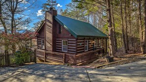 A log cabin with a green roof, wooden deck, and a stone chimney.