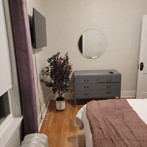 A bedroom with a bed, a dresser, a mirror, and a potted plant.