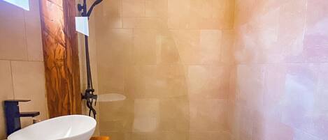 Une salle de bain avec un meuble-lavabo en bois, un lavabo blanc, une douche avec un tuyau noir et un sol carrelé.