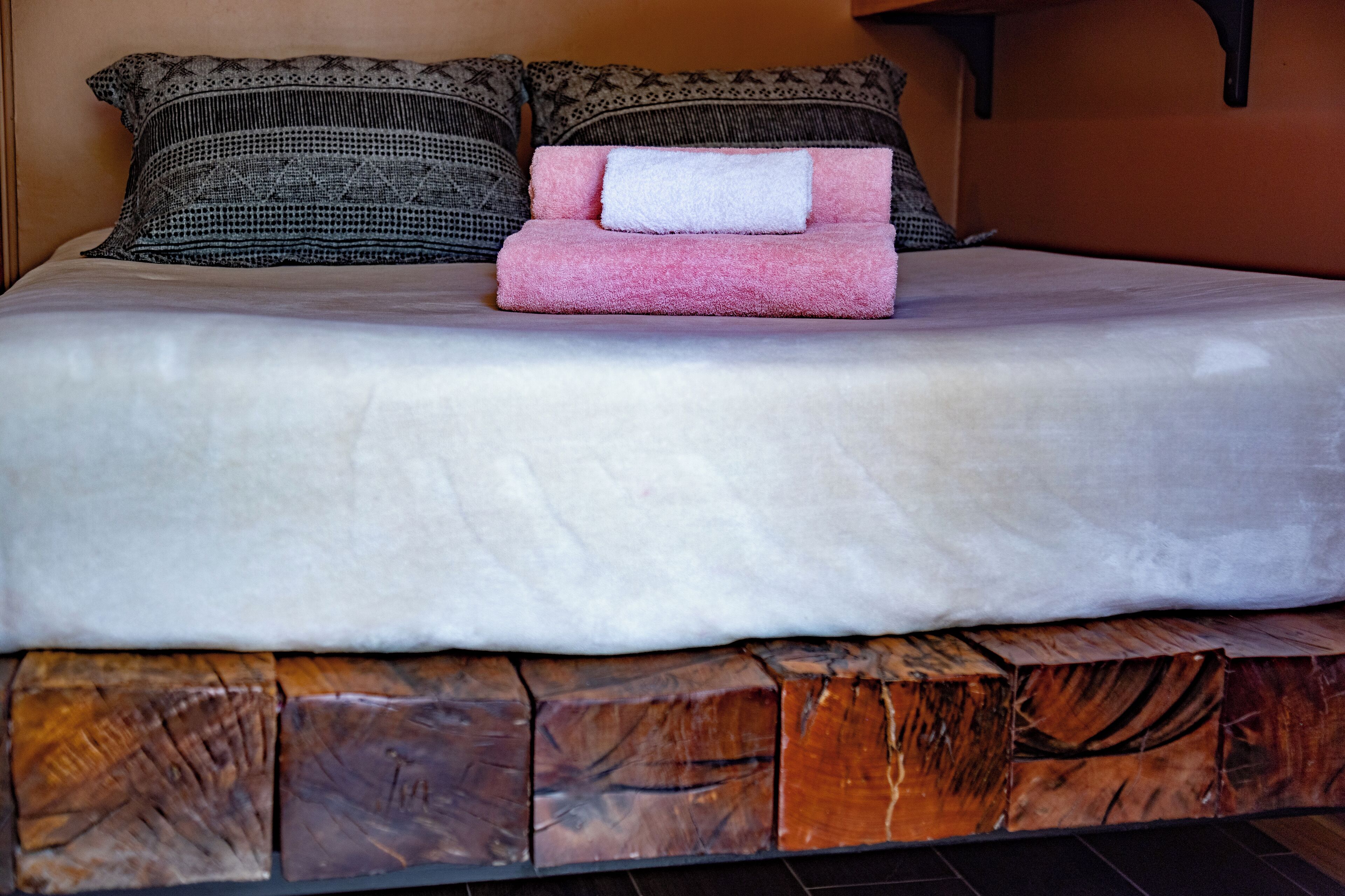 Ein ordentlich bezogenes Bett mit weißer Bettdecke und einem rosa Handtuch, ergänzt durch Kissen mit Muster.