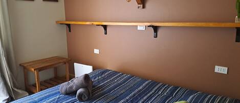 Een slaapkamer met een bed, een houten plank, een klein tafeltje en twee wandlampen.