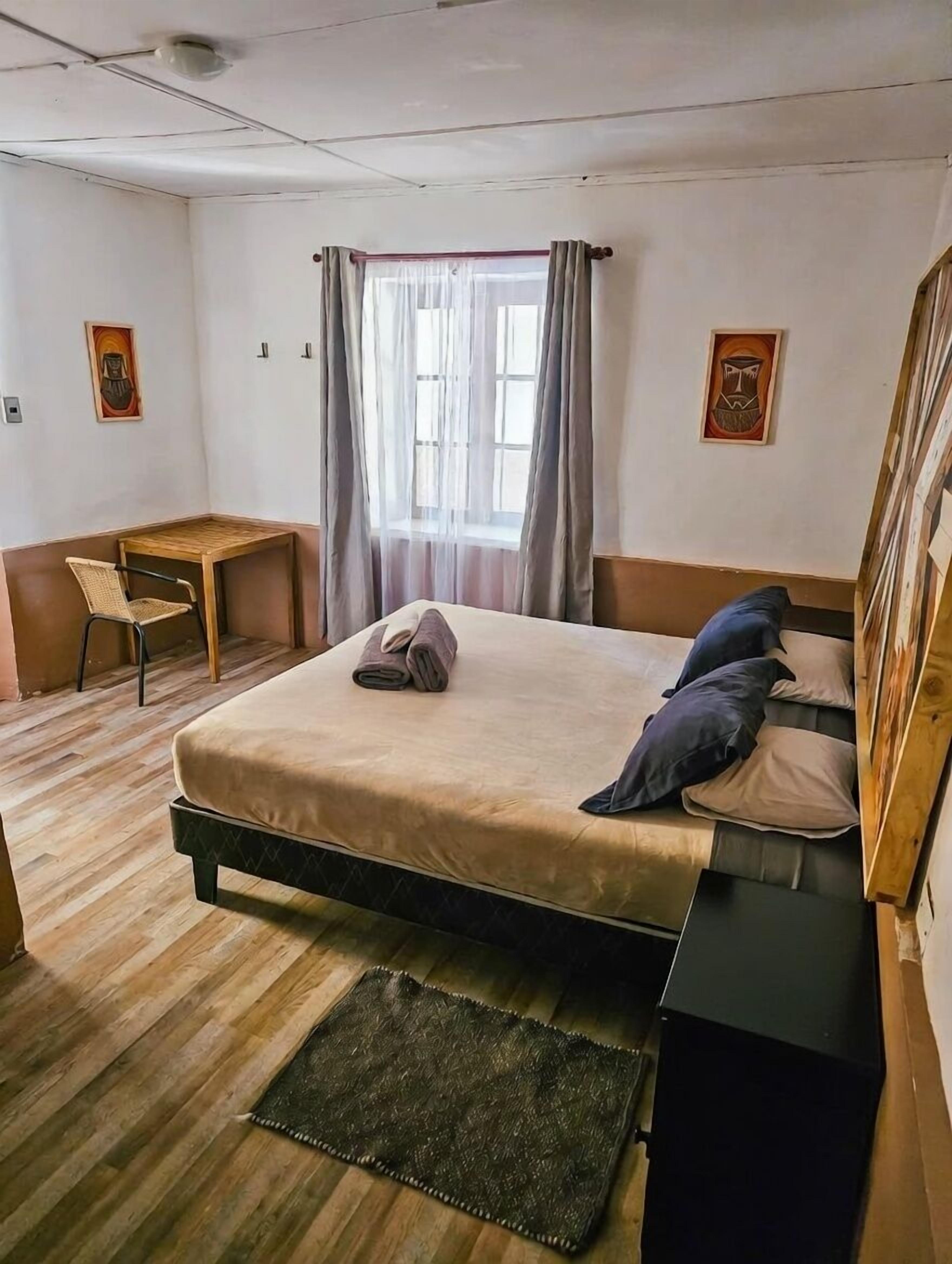 A bedroom with a bed, a desk, a chair, and a window with curtains.