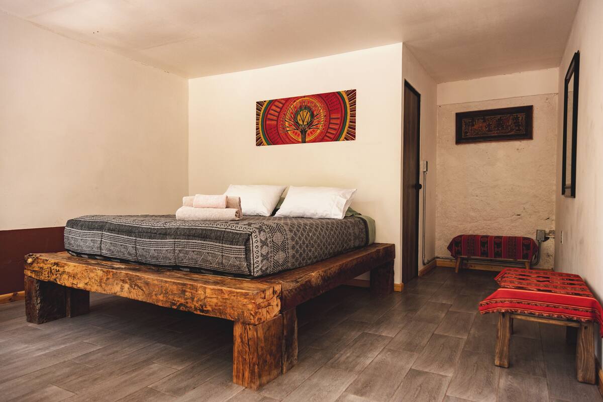 A bedroom with a wooden bed frame, a bench, and a small table.