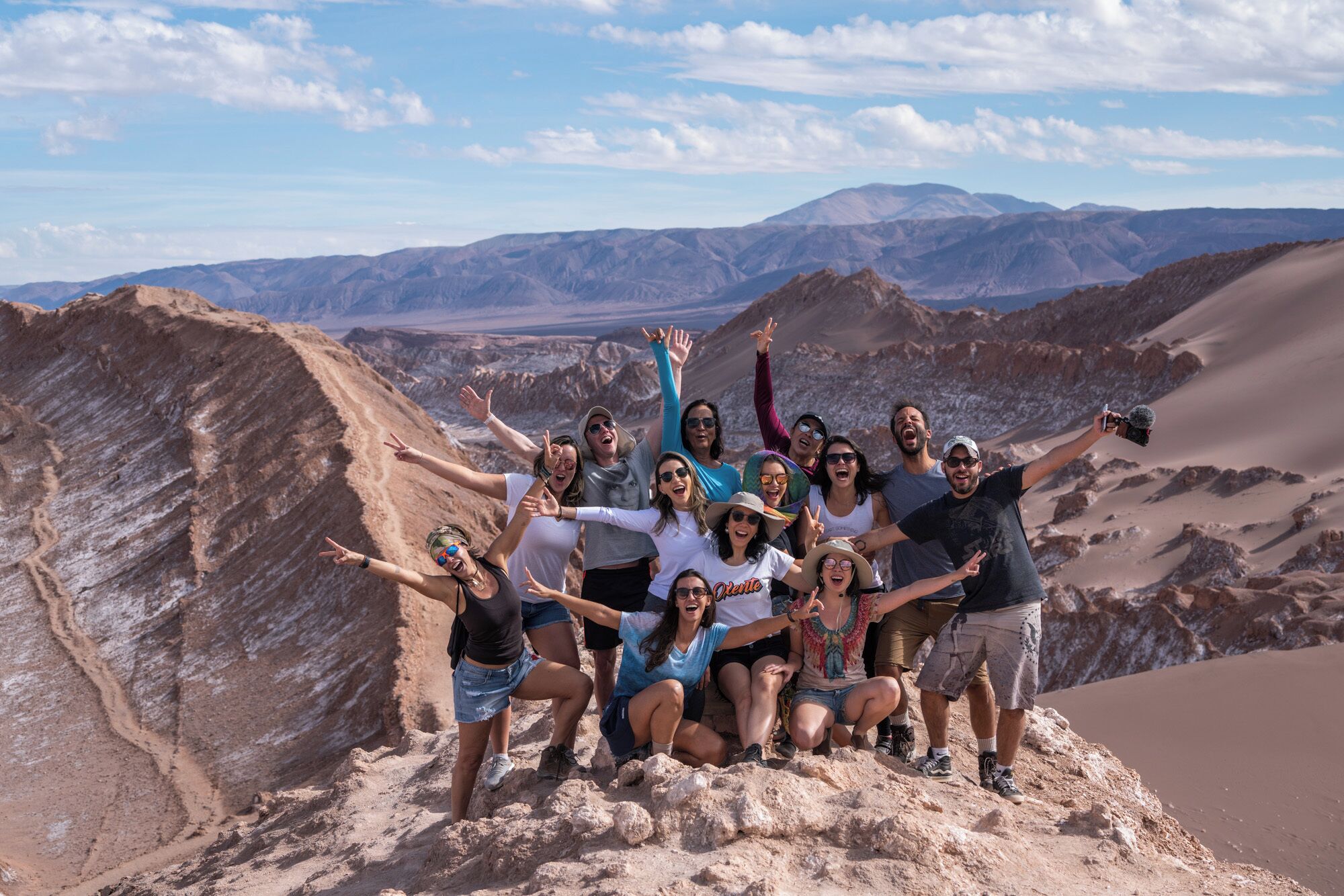 Un grupo de personas posando en una colina arenosa con montañas al fondo.