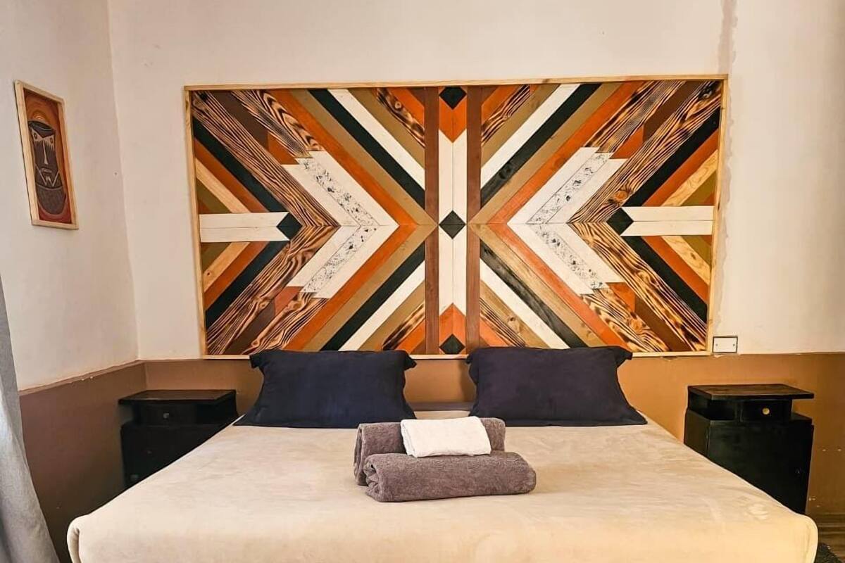 A large bed with a geometric patterned headboard, two bedside tables, and a brown rug on a wooden floor.