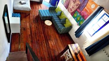 Una habitación con piso de madera, una escalera, un sofá, una mesita y una pared con un mural.