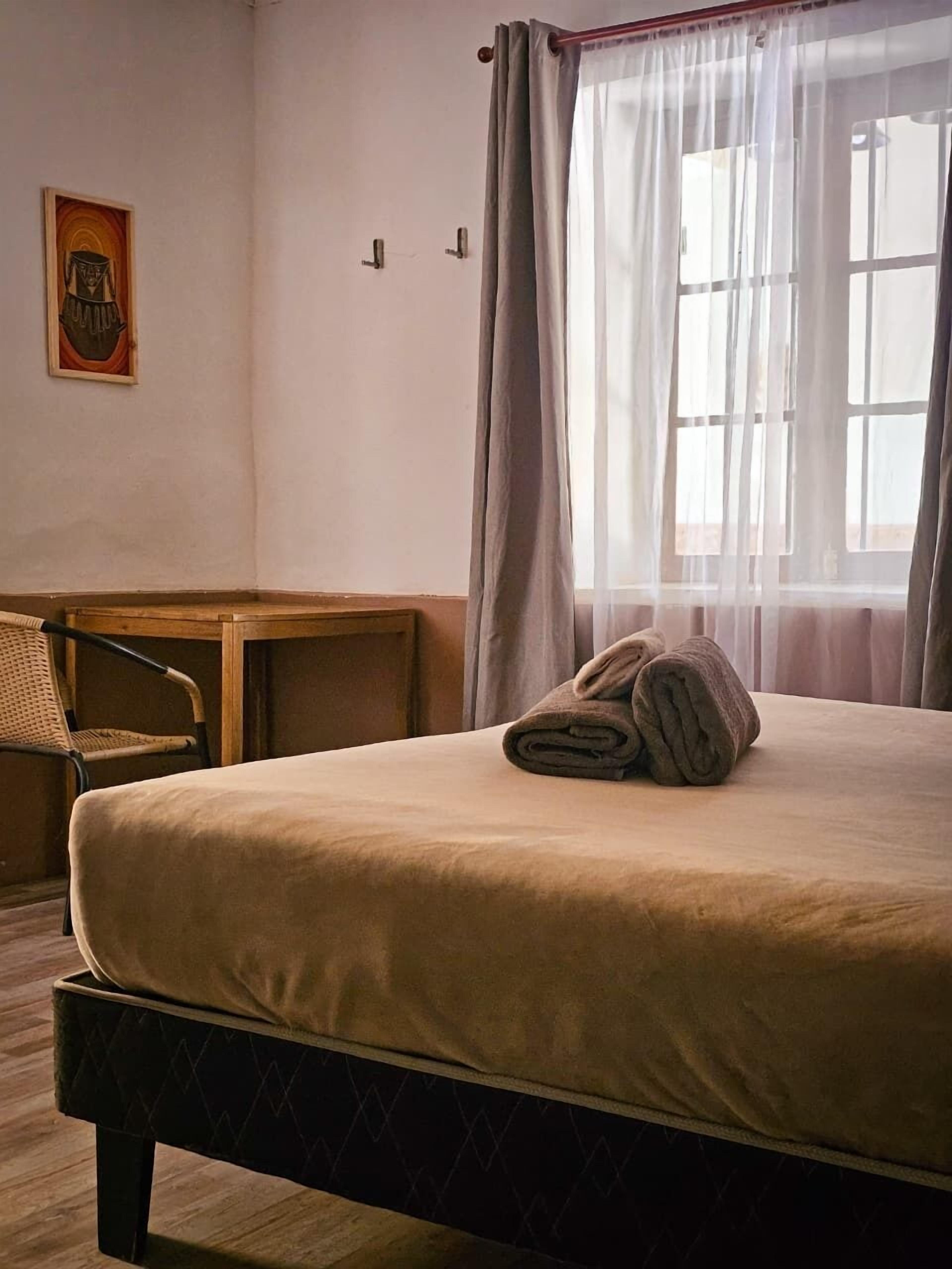 Una habitación de hotel con cama, escritorio, silla y ventana con cortinas.
