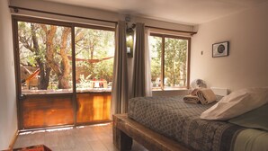 A bedroom with a large bed, a wooden bench, and a view of an outdoor area with trees and a hammock. - Vientos - La Yareta (San Pedro de Atacama)