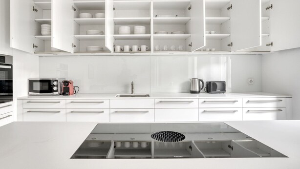 A modern kitchen with white cabinetry, a central island with a built-in range hood, and a microwave on the countertop. - Sleek Vorstädte 3.5 Room w/ W/D & Storage, 2 min to Market, by Blueground (Basel)
