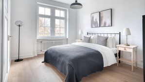 A modern bedroom with a large bed, bedside tables, a floor lamp, and a window with a view. - Sleek Vorstädte 3.5 Room w/ W/D & Storage, 2 min to Market, by Blueground (Basel)