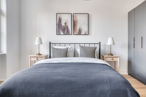 Un dormitorio moderno con una cama grande, dos mesitas de noche y un cabecero. Hay dos obras de arte colgadas en la pared sobre la cama.