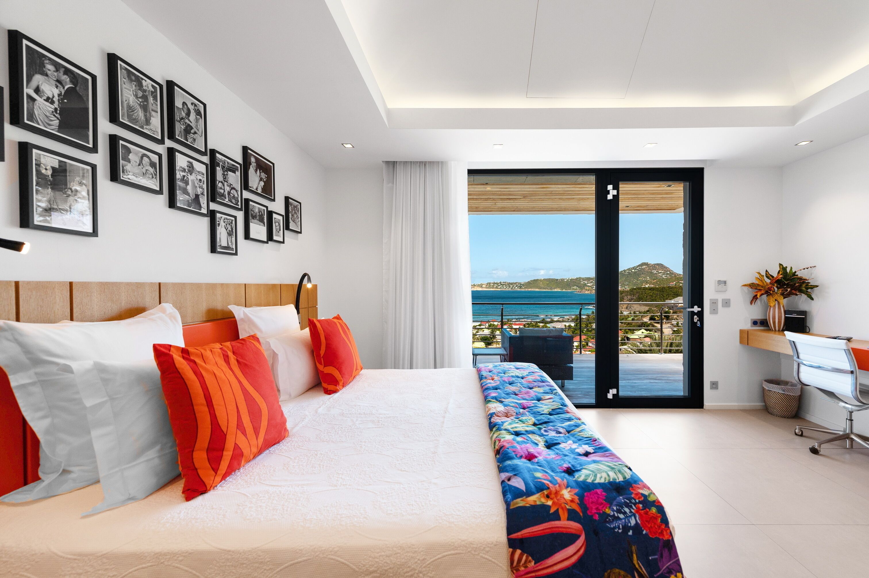 A modern hotel room with a large bed, a desk, and a balcony with a view of the sea.