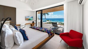 A modern hotel room with a bed, a red armchair, and a large window overlooking the beach. - Villa Grace | Ocean View - Located in  Fabulous Anse des Cayes with Private Pool (Anse des Cayes)