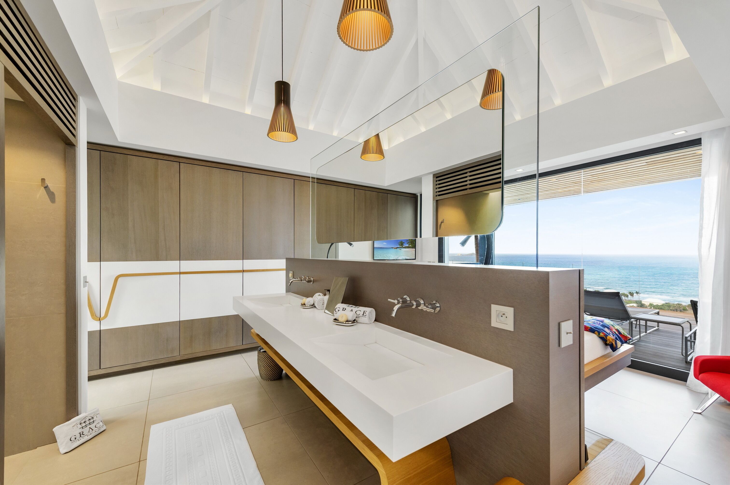 A modern bathroom with a large white sink, wooden cabinets, and a view of the ocean.