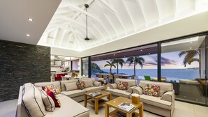 Un salon moderne doté d’un grand canapé, de tables basses et offrant une vue sur l’océan grâce à de grandes fenêtres.