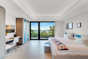 A modern hotel room with a large bed, a desk, and a view of the sea.