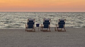 Tres sillas de playa mirando al océano al atardecer.