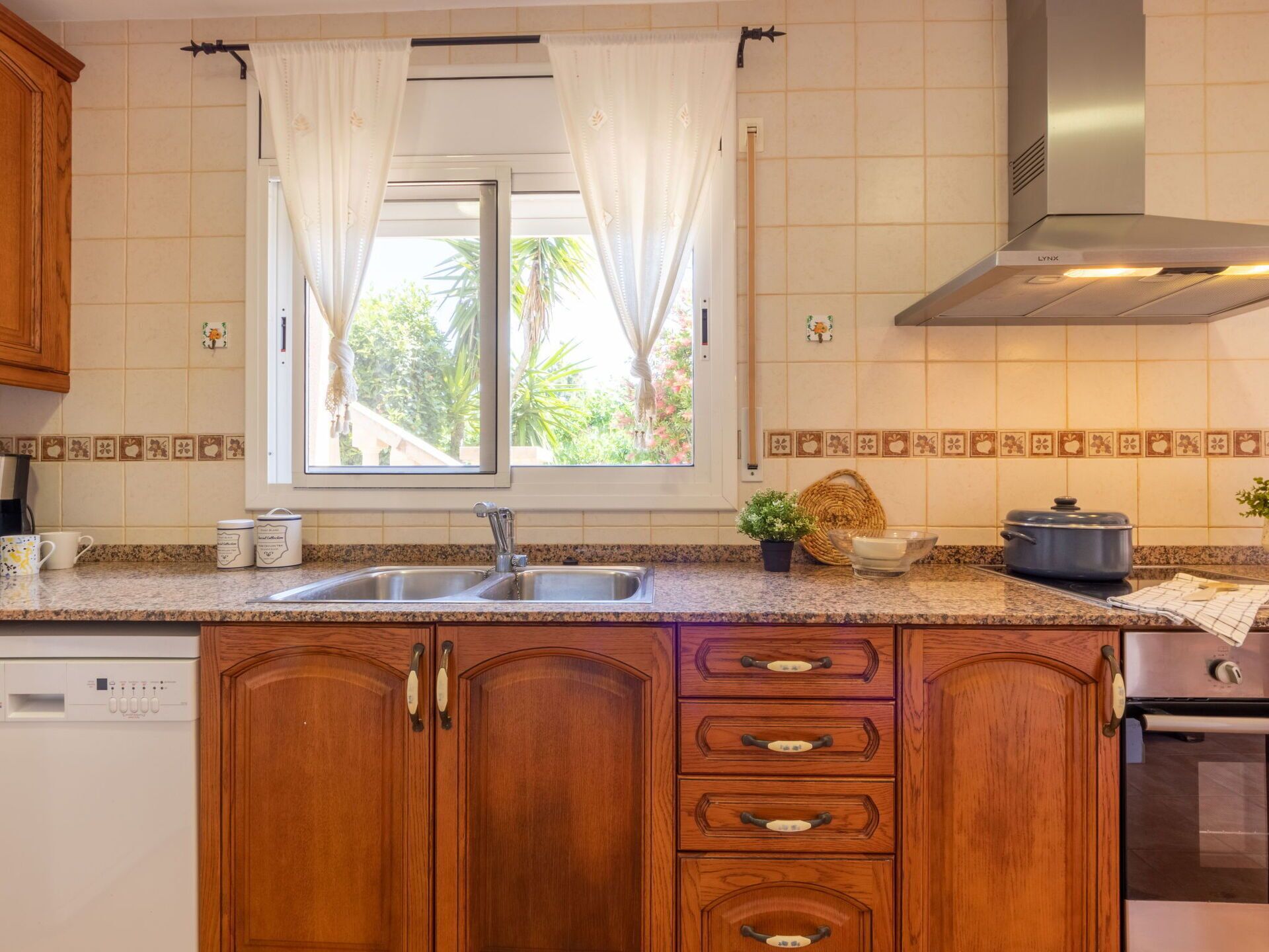 A kitchen with wooden cabinets, a double sink, a stove, and a window with curtains.