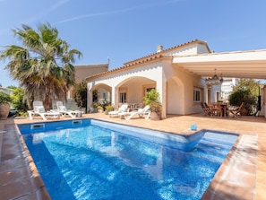 Una piscina con sillas de descanso y una zona de terraza cubierta.