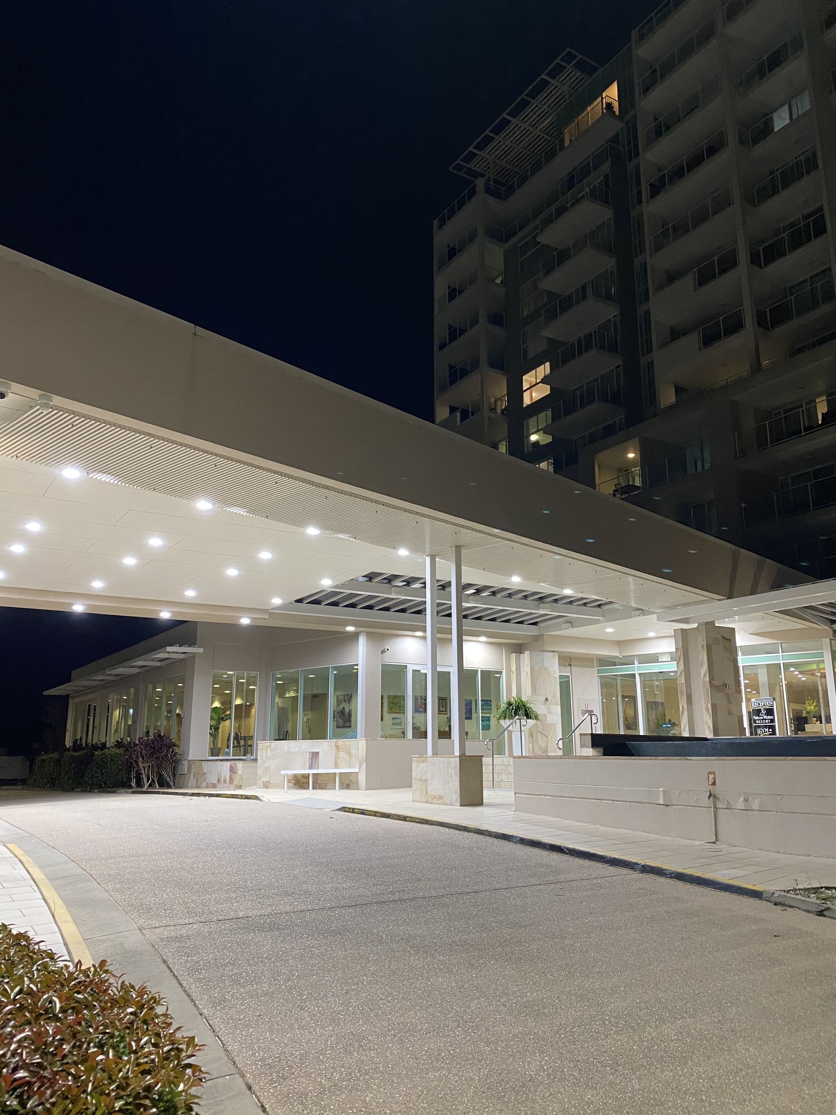 A modern hotel entrance with a covered walkway, large windows, and a parking area.