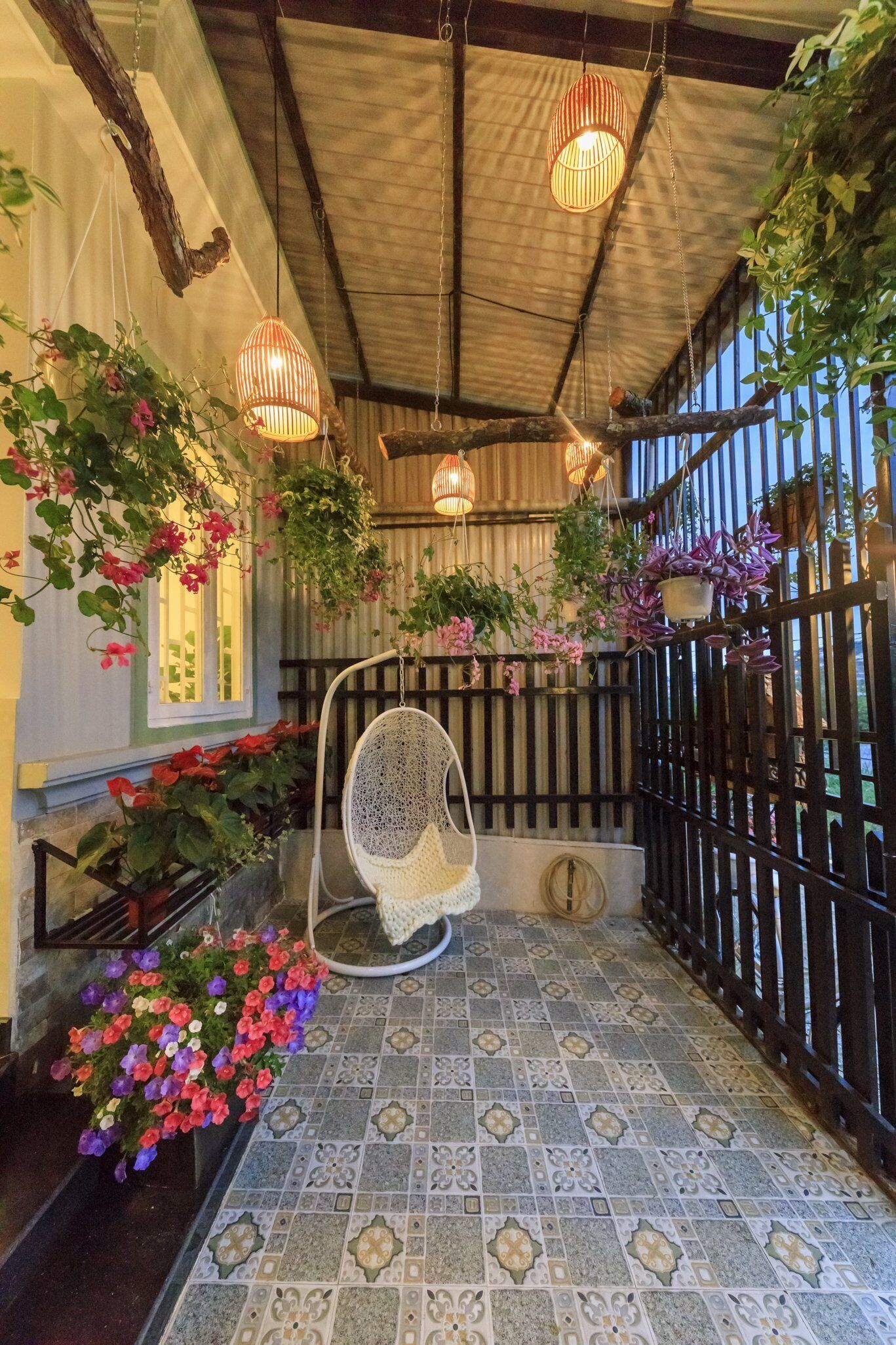 Un espace extérieur abrité, agrémenté de plantes suspendues, d’un fauteuil en osier et de carreaux décoratifs.