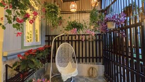 A covered outdoor area with hanging plants, a wicker chair, and patterned tiles. - Chivo House - The House Of Peace (Thành phố Đà Lạt)
