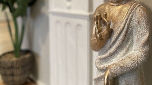 A statue of a seated figure in a traditional pose, likely a religious or cultural symbol, set against a white wall with decorative moldings. - 1.3 miles from Disneyland (Anaheim)