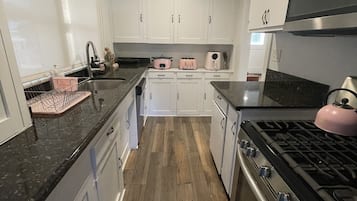 A modern kitchen with white cabinets, a stainless steel stove, and a wooden floor.
