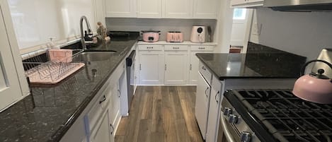 A modern kitchen with white cabinets, a stainless steel stove, and a wooden floor.