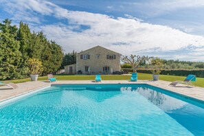 A swimming pool with lounge chairs, a stone building, and surrounding greenery.