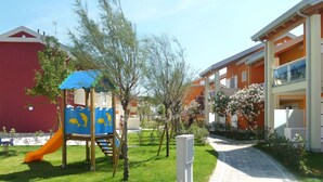 A playground with a slide and climbing structures, surrounded by a well-maintained lawn and trees. - Lovely apartment for 5 people with WIFI, A/C, pool, TV and terrace (Jesolo)