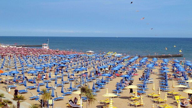 A beach with numerous blue and yellow umbrellas, sun loungers, and a pier extending into the sea. - Lovely apartment for 5 people with WIFI, A/C, pool, TV and terrace (Jesolo)