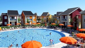 A swimming pool surrounded by colorful buildings with outdoor seating and umbrellas. - Lovely apartment for 5 people with WIFI, A/C, pool, TV and terrace (Jesolo)