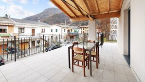 A balcony with a wooden pergola, a glass table with chairs, and a view of buildings and a mountain in the background. - Holiday Apartment "Casa Tovini" with Mountain View, Terrace & Wi-Fi (pisogne)