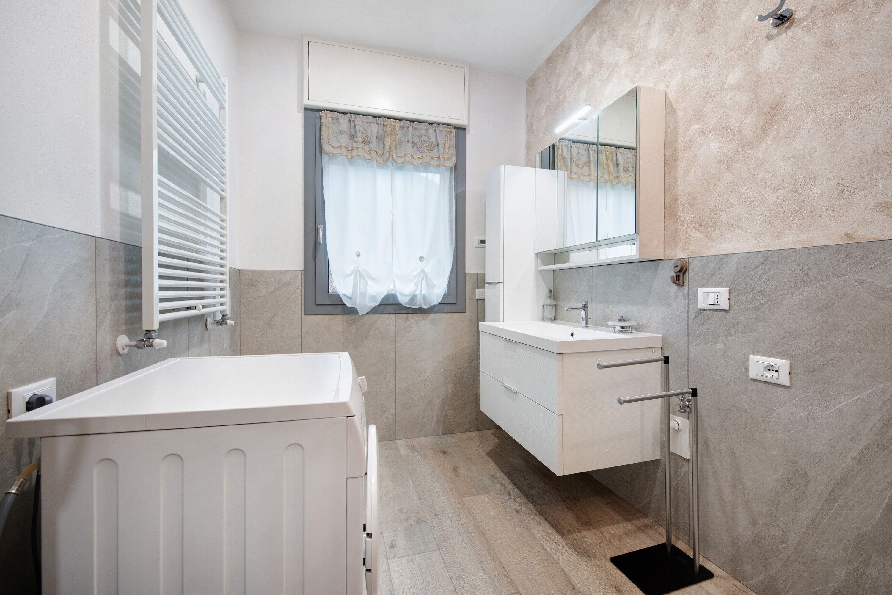 Une salle de bain avec une baignoire, un lavabo, un miroir et une fenêtre avec un rideau.