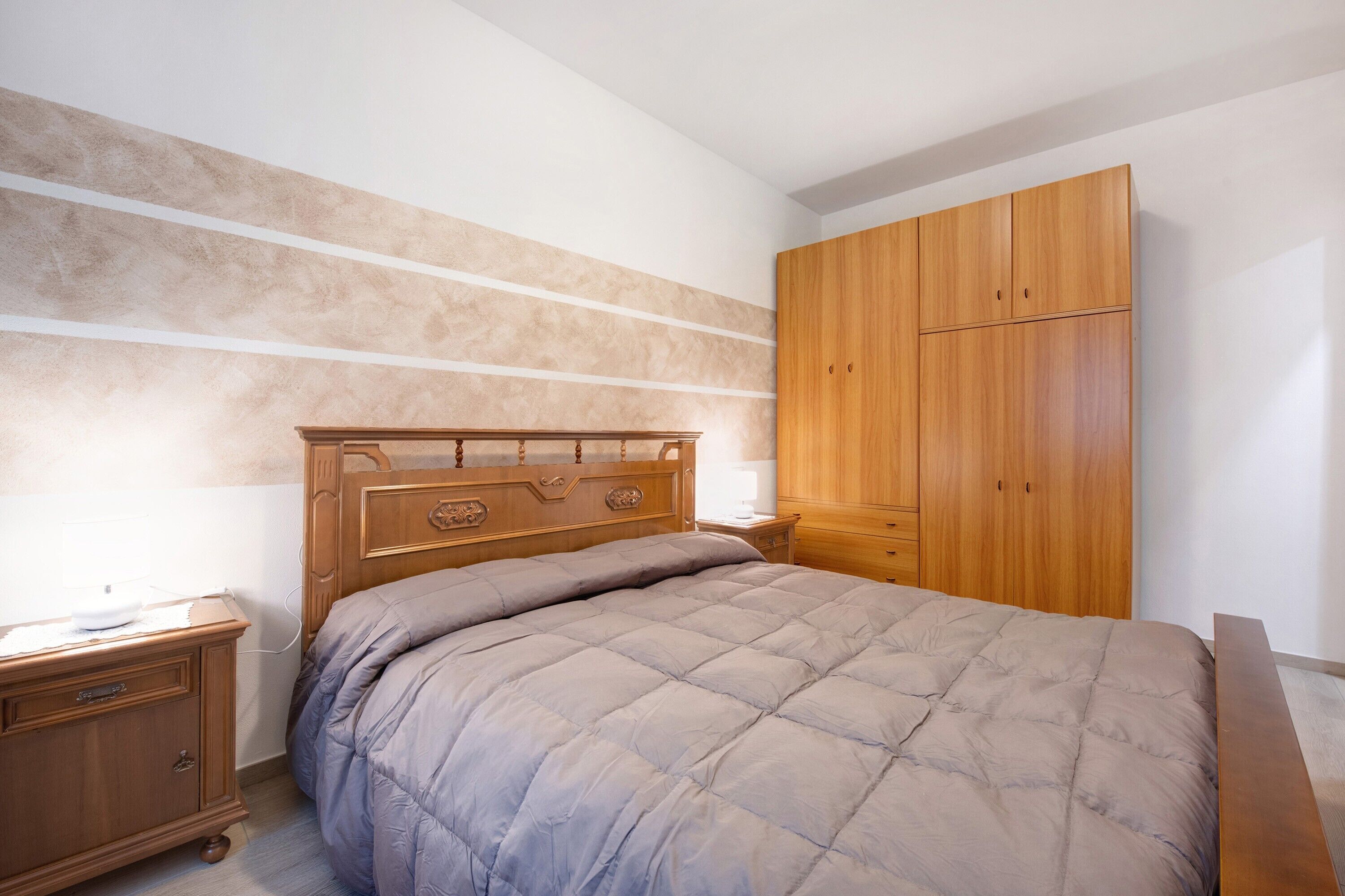 Un dormitorio con cama, armario de madera, mesita de noche y cómoda.