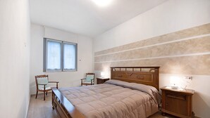 A bedroom with a bed, a wooden nightstand, a chair, and a window. - Holiday Apartment "Casa Tovini" with Mountain View, Terrace & Wi-Fi (pisogne)