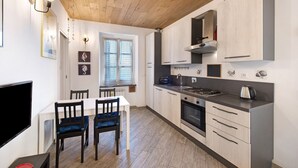 Una cocina moderna con techo de madera, armarios blancos y una zona de comedor con televisor y sillas.