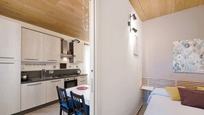 Una cocina compacta con electrodomésticos modernos, un comedor con mesa y sillas, y un dormitorio con cama y mesita de noche.