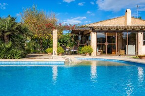 Piscina com área de estar coberta, rodeada por vegetação exuberante e céu azul límpido.